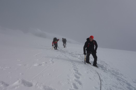 Eine Dreierseilschaft befindet sich auf dem Gletscher im Aufstieg am Piz Palue. Es liegt Schnee und die Sicht ist neblig.