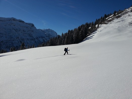 Ein einzelner Skitourengaenger durchquert eine weite Schneeflaeche im Aufstieg zur Marenegg. Strahlender Sonnenschein und blauer Himmel.
