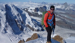 Ein Bergsteiger in roter Jacke auf einem Grat, dahinter ist das Matterhorn erkennbar.